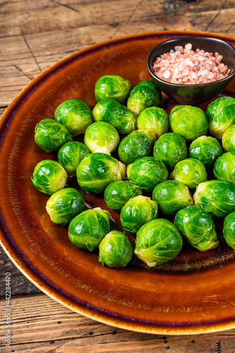 Cooked Brussels green sprouts cabbage in a rustic plate with salt. wooden background. Top view © Vladimir