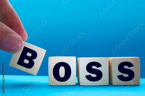 A businessman holds wooden cubes with a word BOSS on a blue background, with space to copy the text, business concept