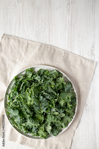Raw Organic Baby Kale on a gray plate on a white wooden background, top view. Flat lay, overhead, from above. Space for text.