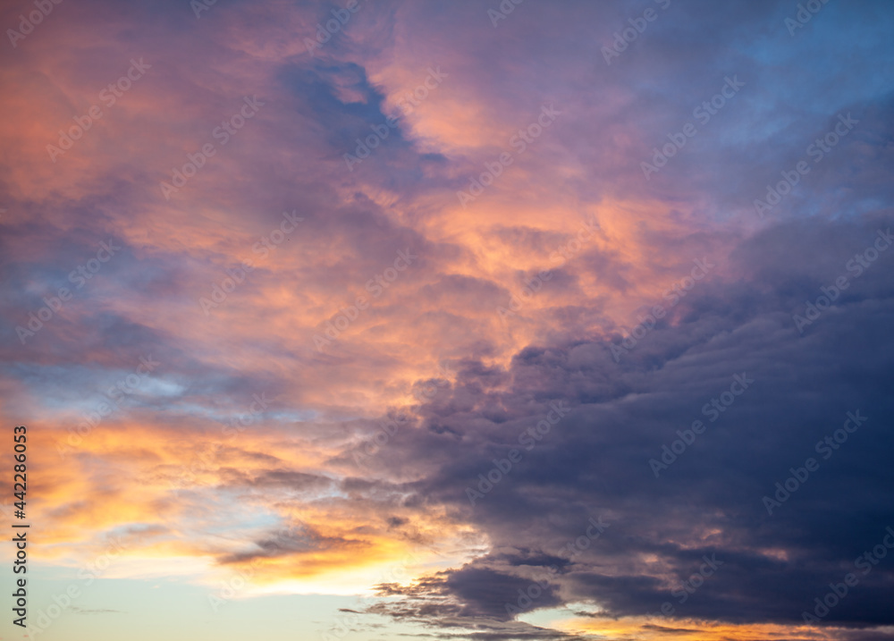 Colorful sunset or sunrise in the sky. The sky and clouds are painted in different bright orange, yellow and blue colors.
