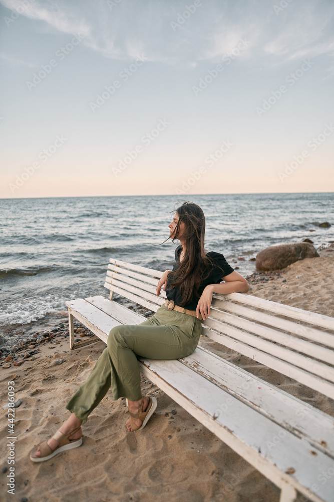 Attractive brunette sits on the sand beach. Concept of serenity at the beautiful place near the sea