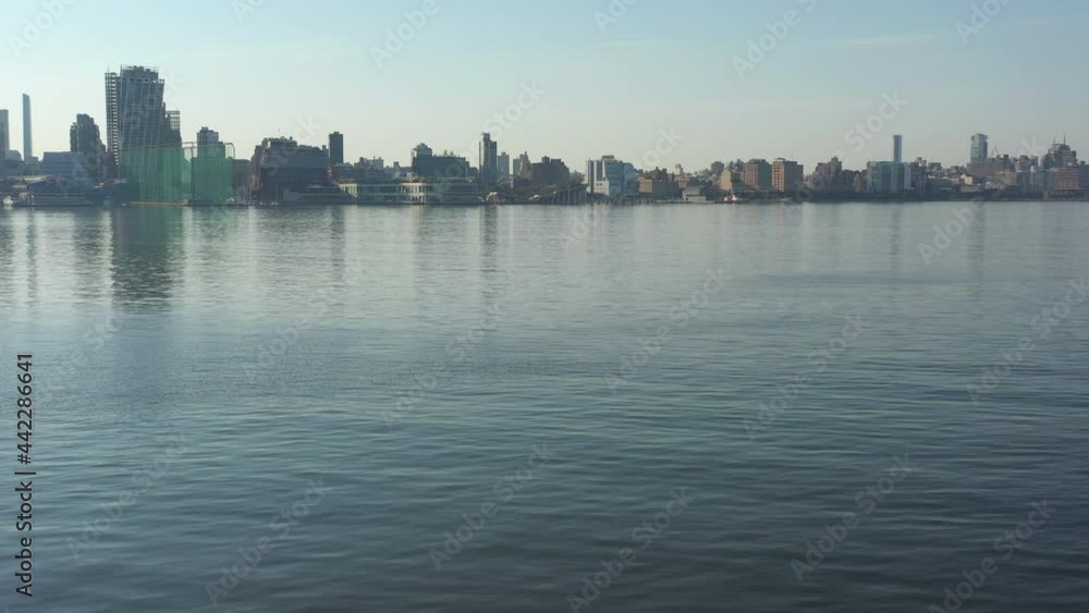 A low angle drone shot over a calm Hudson River at sunrise. The camera dolly in over the water flying low, towards the west side of Manhattan, NY. A low angle drone shot over a calm Hudson River at sunrise. The camera dolly in over the water flying low, towards the west side of Manhattan, NY.