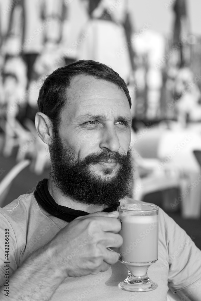 Black and white portrait of handsome bearded man drinking hot, morning espresso coffee with milk looks into the distance In sunset lighting. concept with space for text. Man Holding A Coffee Mug Black and white portrait of handsome bearded man drinking hot, morning espresso coffee with milk looks into the distance In sunset lighting. concept with space for text. Man Holding A Coffee Mug