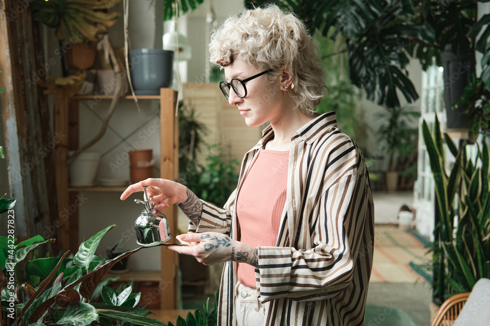 Young woman in eyeglasses caring about plants and waterig them in the garden