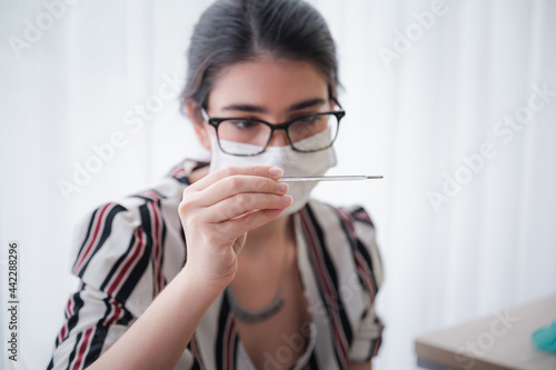 Young woman wearing a mask looking at a thermometer. After vaccination against coronavirus 19 to immunize in the laboratory Concept of protecting against COVID-19 virus