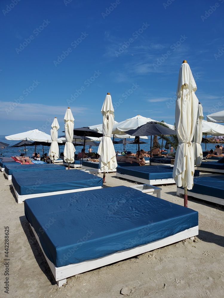 Obraz premium Beach furniture on summer beach. Empty beds and white textile sun shades on beach sand. Luxury coastal vacation