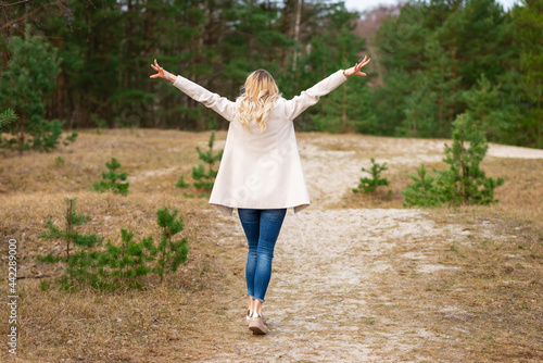 One young beautiful blonde long haired woman with raised hands over green natural forest background outdoor.