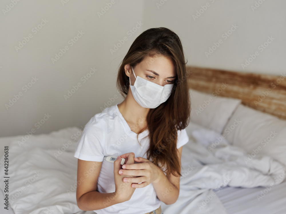 woman sitting in bed with thermometer under her arm checking temperature