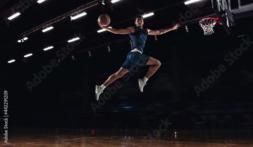 Young African sportsman, basketball player jumping high isolated on dark background. Concept of sport, game, competition. Dynamic
