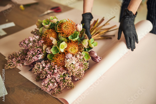 Woman in disposable nitrile gloves wrapping a mixed flower bouquet photo