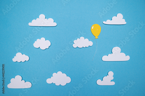 Paper cut out balloons floating through a blue sky and fluffy white clouds photo