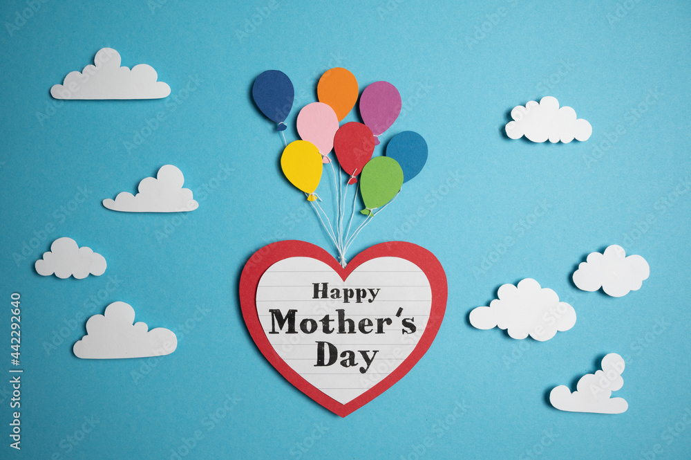 Balloons lift a big paper heart with Happy mother´s day text on it through a blue sky and fluffy white clouds