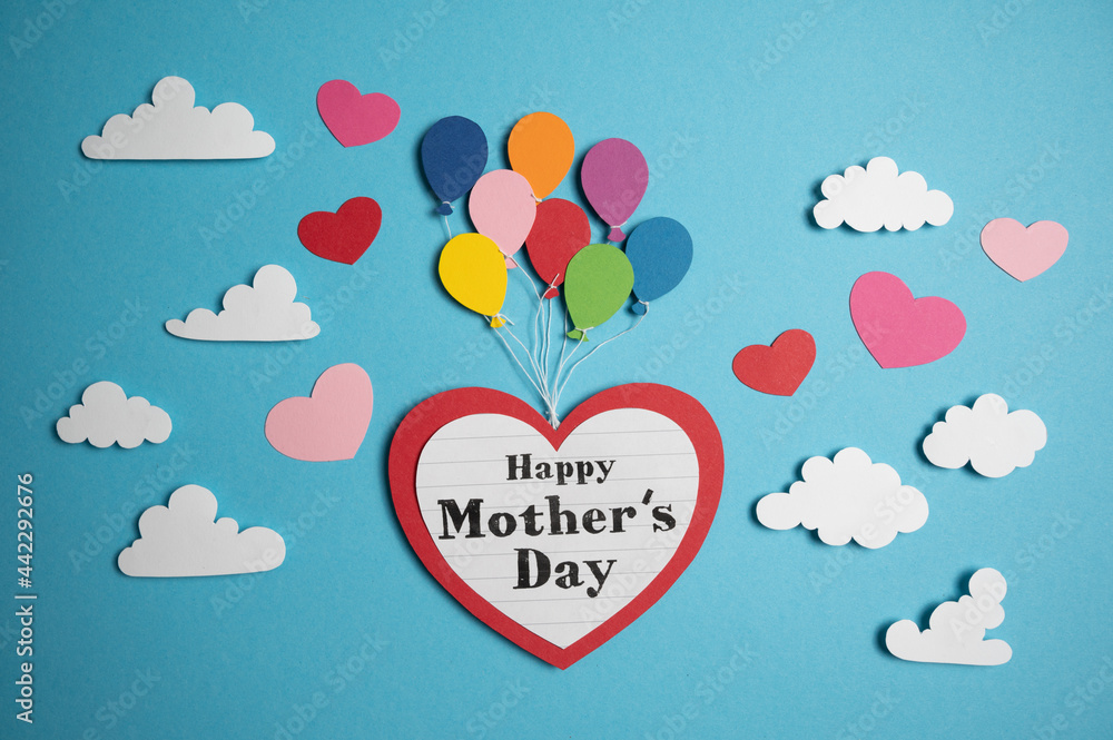 Paper cutout Balloons lift a big heart with Happy mother´s day text on it through a blue sky and fluffy white clouds. small pink paper hearts flitter away