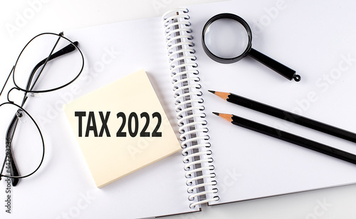 Word TAX 2022 on the sicker on the notebook with pencils,magnifier and glasses photo