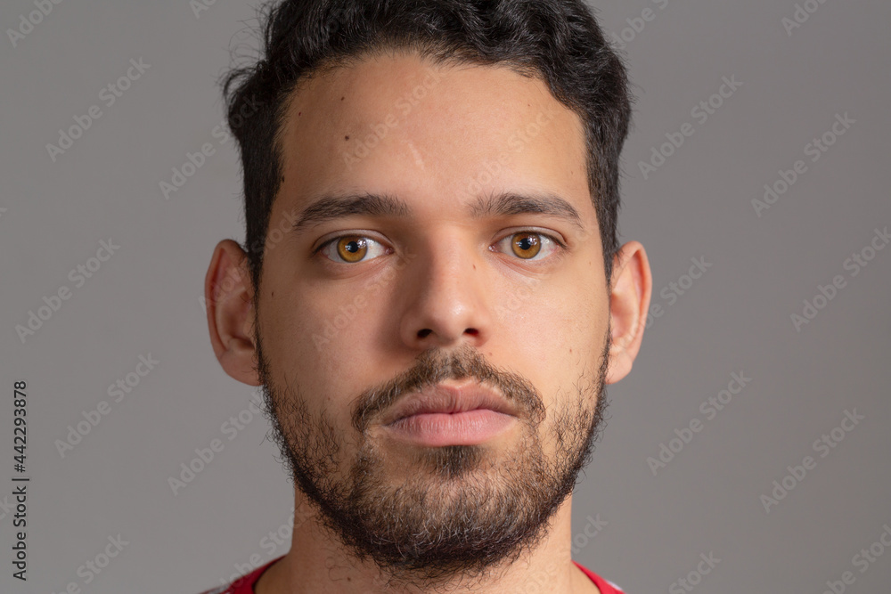 Naklejka premium Young man frontal extreme closeup portrait in a studio shot, He is latin in his 20s. He is serious.