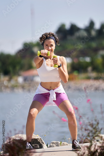 Fototapeta Naklejka Na Ścianę i Meble -  Portrait of athlete strong woman in white dress holding dumbbells