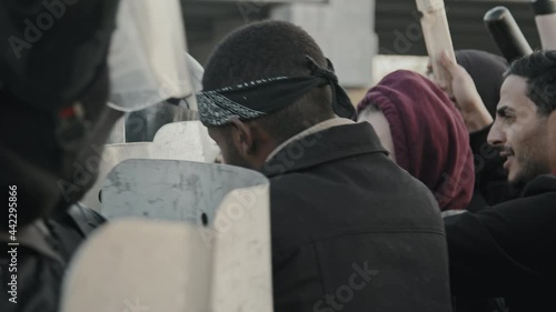 Handheld slowmo shot of young protesters pushing against riot police shields