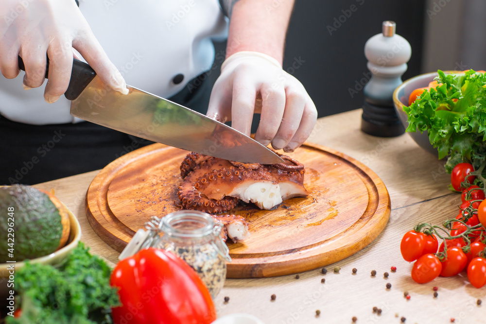 Young chef is cutting octopus in a modern kitchen. The man prepares food at home. Cooking healthy and tasty food.