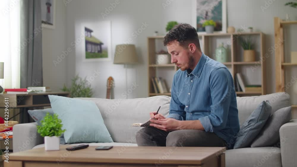 A young pretty man draws a pencil in a sketchbook. Male one house in the living room. Designer at work. A young pretty man draws a pencil in a sketchbook. Male one house in the living room. Designer at work.