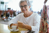 Attractive traveler smiling woman in airport waiting for boarding drinks a coffee cup looking at camera. Elderly white haired lady enjoying journey