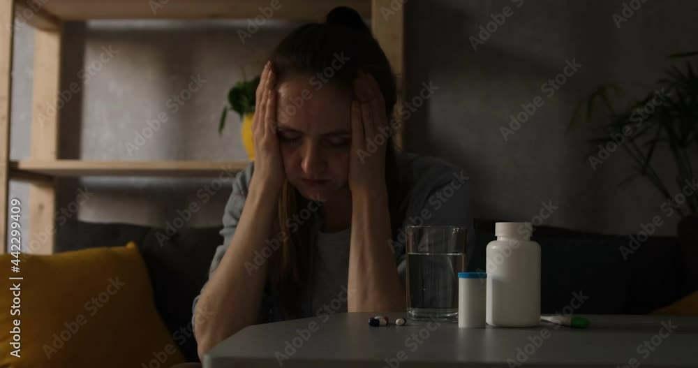 Young woman looks pretty sick sitting near pills. Girl with depression holds head in hands. Young woman looks pretty sick sitting near pills. Girl with depression holds head in hands.
