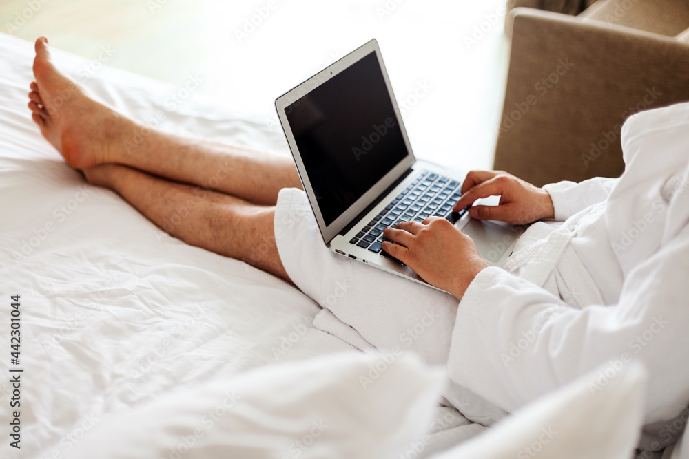 a man in a robe lies on a bed with a computer on his feet. Freelance, work from home. No face. A man in a hotel, working in a bedroom at a computer. a man in a robe lies on a bed with a computer on his feet. Freelance, work from home. No face. A man in a hotel, working in a bedroom at a computer.