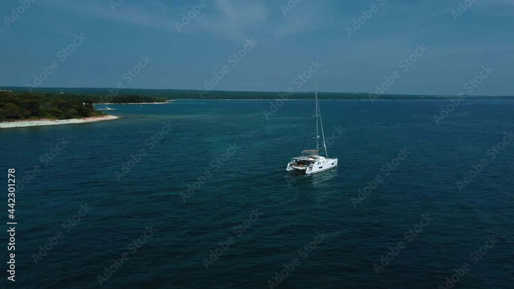 A catamaran sailing ship boat in a blue clear water seaside bay in the idyllic vacation Adriatic mediterranean sea ocean close to the Croatian coast with blue sky. Drone aerial holiday footage A catamaran sailing ship boat in a blue clear water seaside bay in the idyllic vacation Adriatic mediterranean sea ocean close to the Croatian coast with blue sky. Drone aerial holiday footage