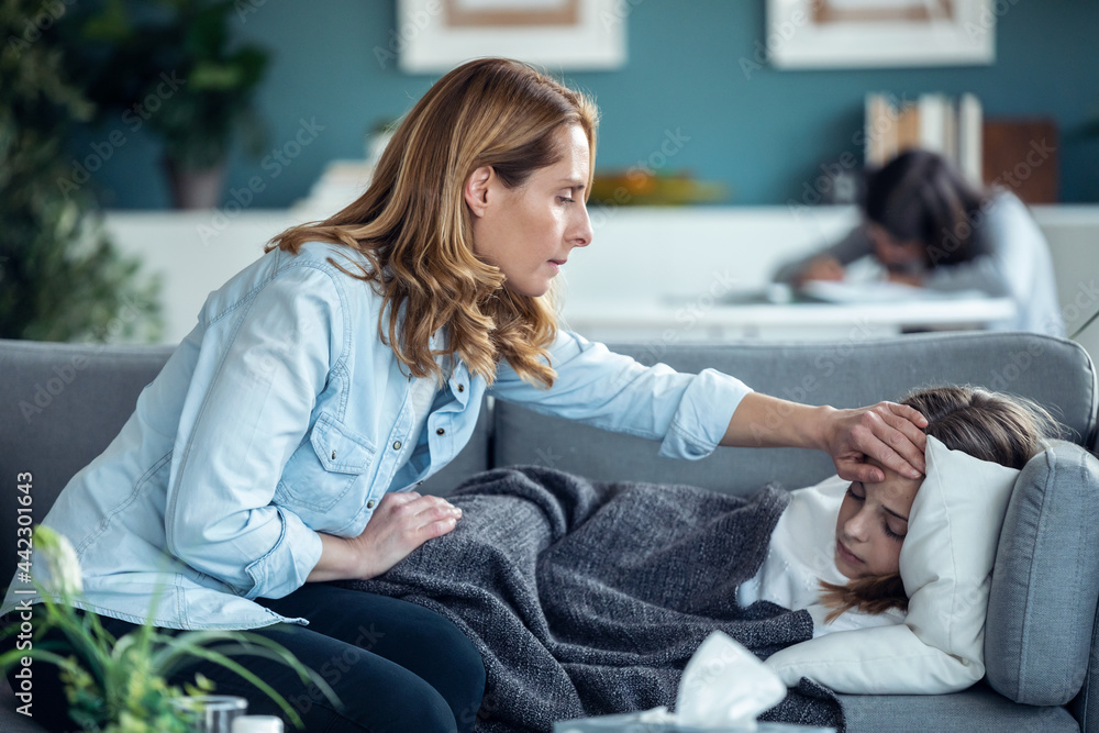 Mature mother caring for her sick daughter while she rests on the sofa in living room at home. Mature mother caring for her sick daughter while she rests on the sofa in living room at home.