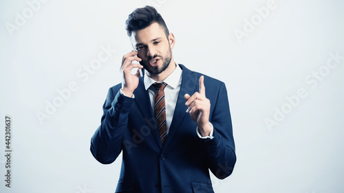serious businessman pointing up with finger while calling on smartphone isolated on white