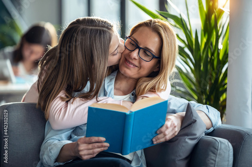 Mature beautiful woman reading a book while her daughter hugging in living room at home. photo