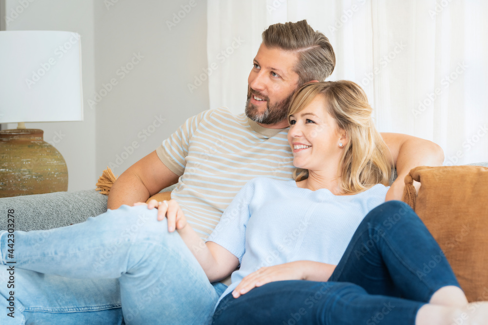 Shot of an affection couple relaxing together in their living room at home. Handsome man watching tv while her beautiful wife napping next to him. Shot of an affection couple relaxing together in their living room at home. Handsome man watching tv while her beautiful wife napping next to him.