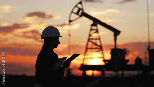 Silhouette female engineer hard at work in oilfield by pump. Woman engineer at the oil pump with a tablet.