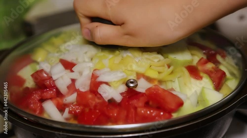 A female hand closes the lid in a frying pan, frying zucchini and carrots, tomatoes, peppers. Cooking food at home. Preparation for frying