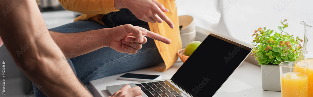 partial view of young couple pointing with fingers at laptop at home, banner