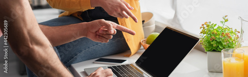 partial view of young couple pointing with fingers at laptop at home, banner