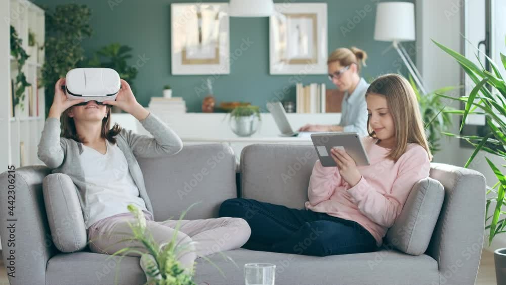 Video of little girl using virtual reality headset while her mother and sister working in living room at home. Video of little girl using virtual reality headset while her mother and sister working in living room at home.