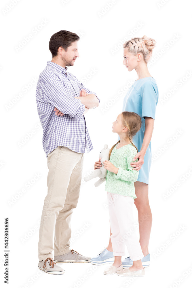 Vertical full length shot of little girl standing with her father and mother watching them quarrelling about something, white background