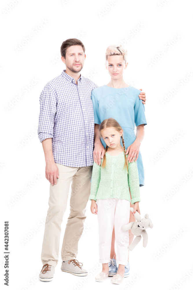 Vertical full length shot of young adult parents wearing casual clothes standing with their sad little daughter, white background Vertical full length shot of young adult parents wearing casual clothes standing with their sad little daughter, white background