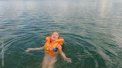 the child a girl in a life jacket swims in the water