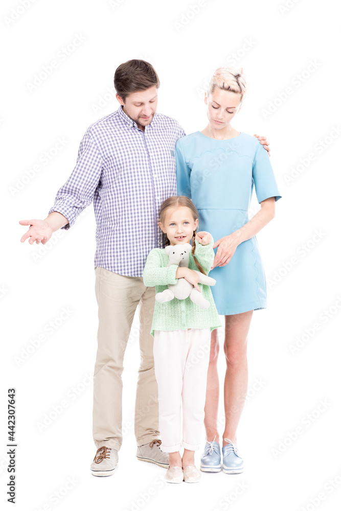 Vertical full length shot of little Caucasian girl showing something to her parents pointing finger at camera, white background Vertical full length shot of little Caucasian girl showing something to her parents pointing finger at camera, white background