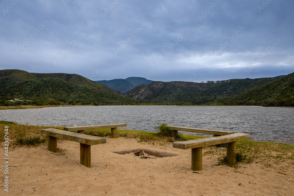 Four wooden benches on a beach with water and hills in the back ground.