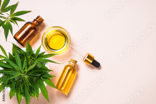 Cannabis oil hemp oil in glass bowl and cosmetic bottles with dropper and fresh leaves at pastel background. Flat lay image with copy space.