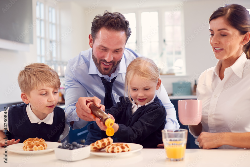 Children Wearing School Uniform In Kitchen Eating Breakfast Waffles As Parents Get Ready For Work Children Wearing School Uniform In Kitchen Eating Breakfast Waffles As Parents Get Ready For Work