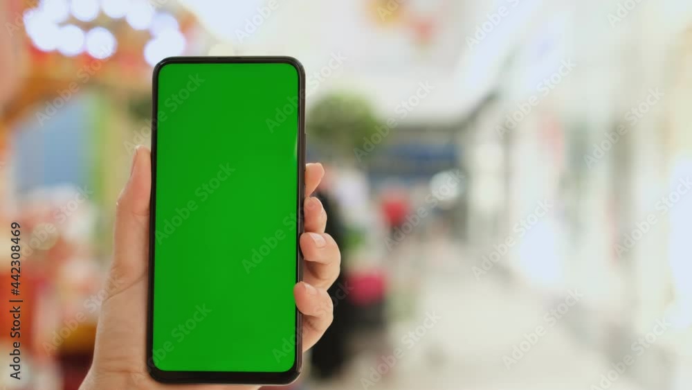 Mall. Shopping center. Back view of brunette holding chroma key green screen smartphone watching content. Shopping online. Gadgets and contemporary people concept. Mall. Shopping center. Back view of brunette holding chroma key green screen smartphone watching content. Shopping online. Gadgets and contemporary people concept.