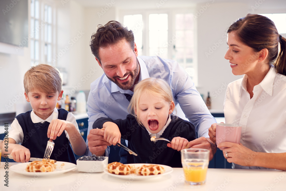 Children Wearing School Uniform In Kitchen Eating Breakfast Waffles As Parents Get Ready For Work
