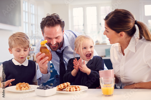 Children Wearing School Uniform In Kitchen Eating Breakfast Waffles As Parents Get Ready For Work