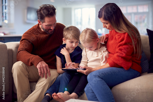 Family Sitting On Sofa Watching Digital Tablet Together