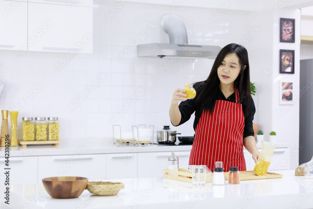 Delighted ethnic female in apron standing with assorted ingredients in kitchen while cooking lunch and looking at camera Delighted ethnic female in apron standing with assorted ingredients in kitchen while cooking lunch and looking at camera