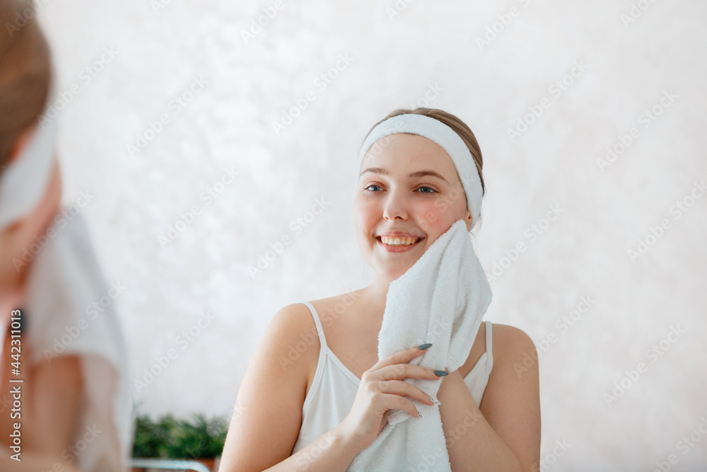 Young woman wipes herself face with white towel after shower washing. Self care in morning at bathroom. Happy smiling teenage girl do morning routine daily hygiene. Portrait reflection in mirror Young woman wipes herself face with white towel after shower washing. Self care in morning at bathroom. Happy smiling teenage girl do morning routine daily hygiene. Portrait reflection in mirror