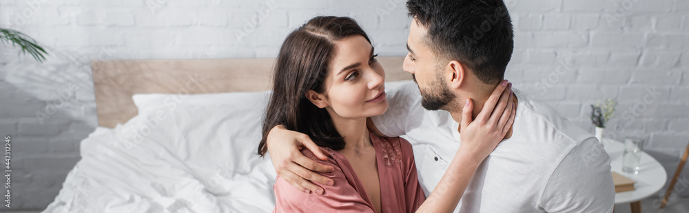 smiling young couple gently hugging and looking at each other in bedroom, banner